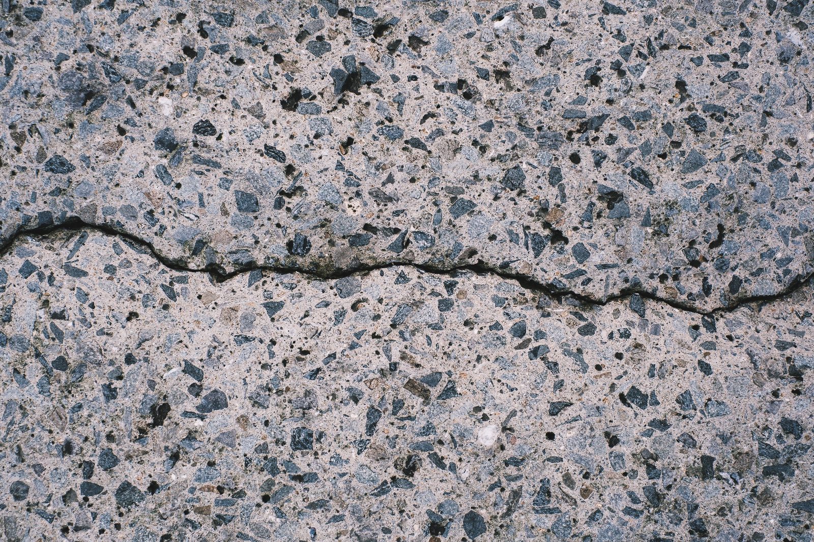 Cracked exposed aggregate driveway surface needing resin resurfacing